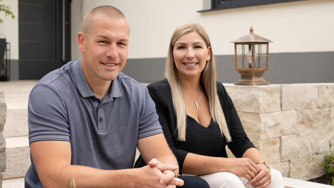 Zwei Immobilienmakler aus Baunatal sitzen auf einer Steintreppe im Garten eines Einfamilienhauses